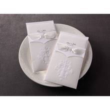 Two traditional embossed pocket invitation side by side showcasing white ribbon and intricate pattern embossing